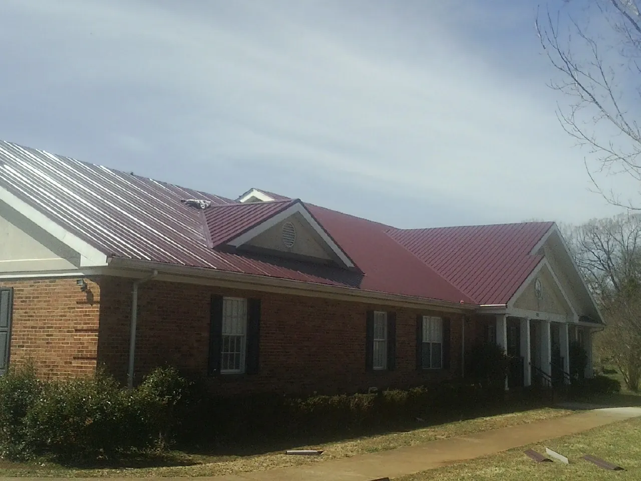 Red metal roof with gabled entries on a long brick building, from a Hail Damage Roof Repair job in Fernandina Beach