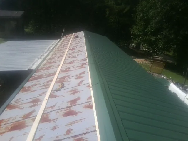 Old rusted panels beside newly installed green metal roofing — Wind Damage Roof Repair by Roofing Brothers in Fernandina Beach