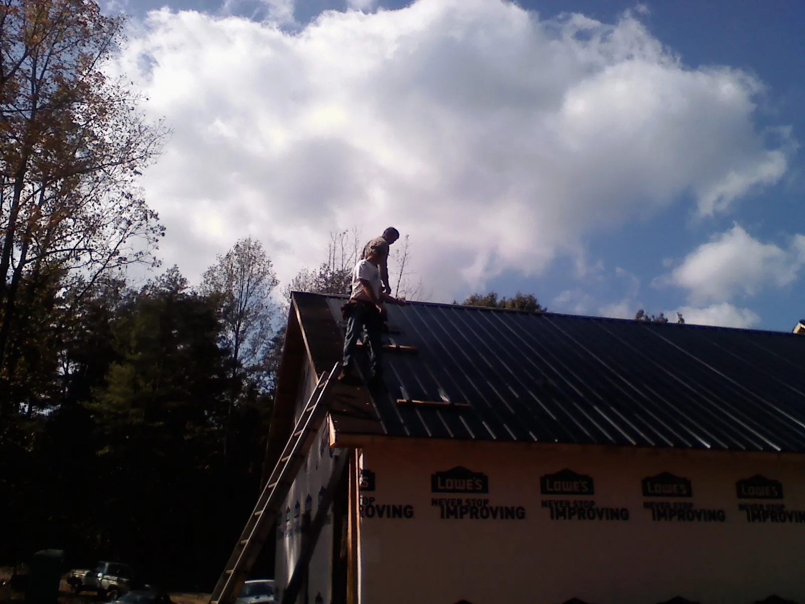 Roofer fastening dark metal panels high against a cloudy sky, from a Roof Inspection job in Fernandina Beach