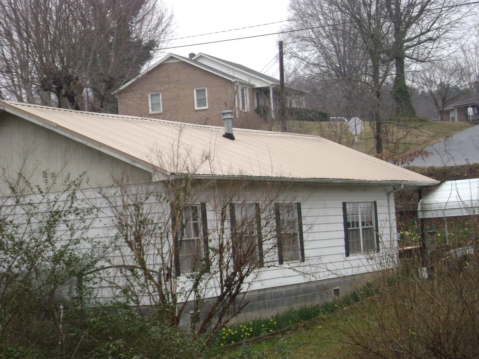 Tan metal roof on a white sided house set into a hillside — Commercial Roofing by Roofing Brothers in Fernandina Beach
